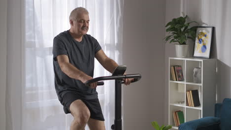 morning-cardio-training-on-exercise-bicycle-middle-aged-man-is-doing-sport-in-his-living-room-at-weekend-sitting-on-exercycle